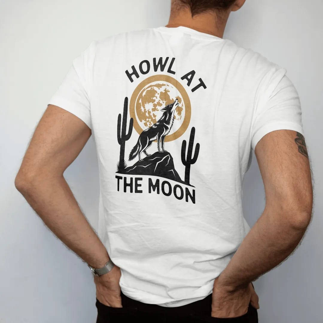Man wearing a White tee, seen from the back: a coyote on a rock howling at a big full moon with saguaros below, "HOWL AT" in small retro 70s caps above and "THE MOON" below, in a faded 1970s souvenir style with a worn cracked-ink texture, printed…