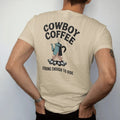 Man wearing a Sandstone tee, seen from the back: vintage ad parody of an enamel coffee pot over a campfire with steam, "COWBOY COFFEE" in a banner of chunky rounded 70s letters and "STRONG ENOUGH TO RIDE" small below, in a faded 1970s souvenir…