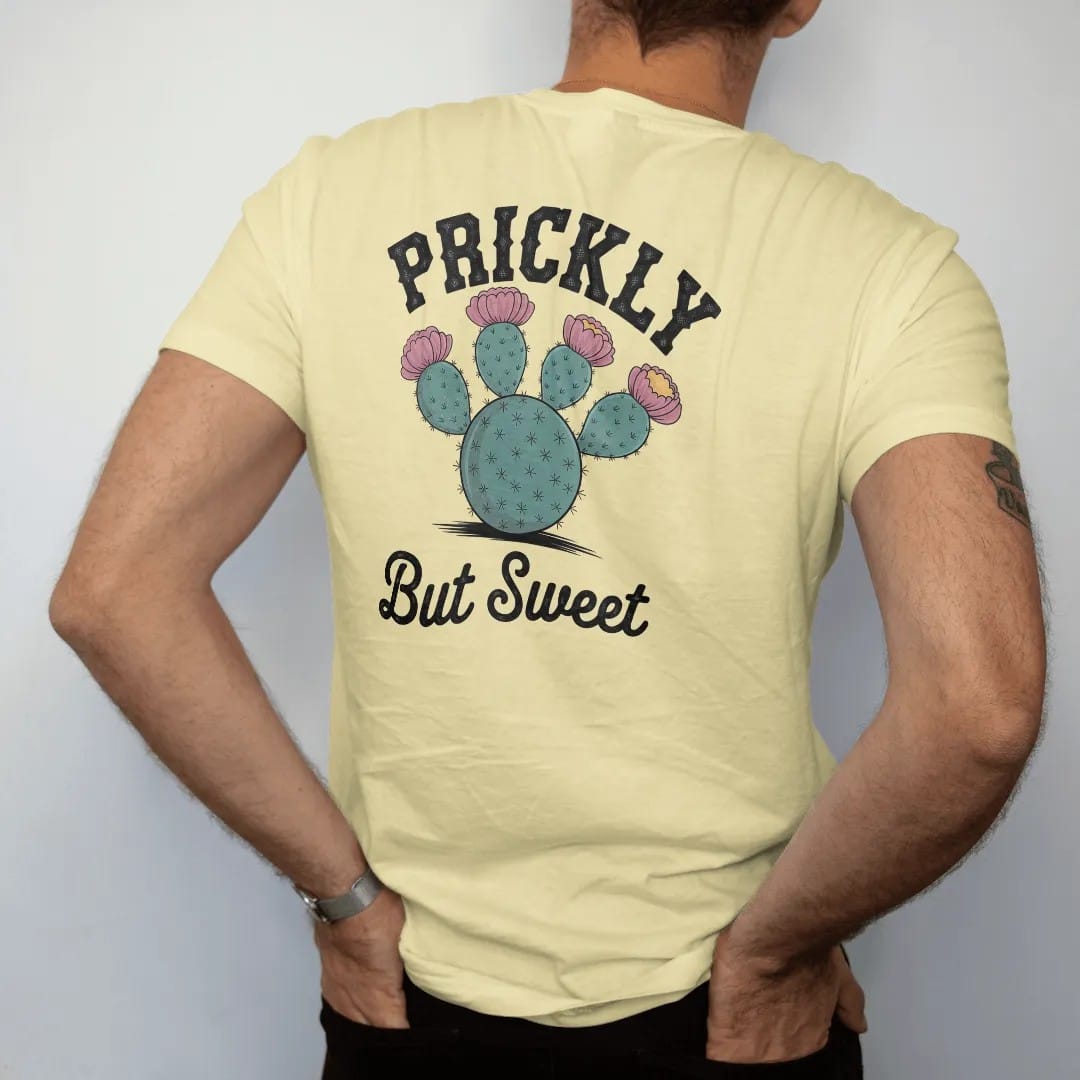Man wearing a Butter tee, seen from the back: a round prickly pear cactus with bright blooms and fruit, "PRICKLY" in chunky 70s block letters above and "BUT SWEET" in a looping 70s rope script below, in a faded 1970s souvenir style with a worn…