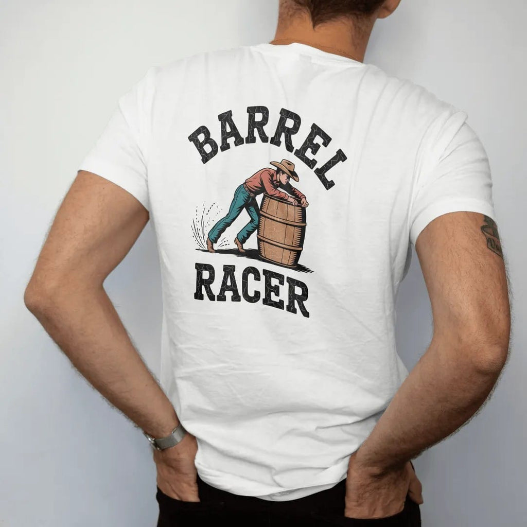 Man wearing a White tee, seen from the back: a barrel racer leaning hard around a barrel with dust flying, "BARREL" arched above and "RACER" below in chunky 70s slab letters, in a faded 1970s souvenir style with a worn cracked-ink texture, printed…