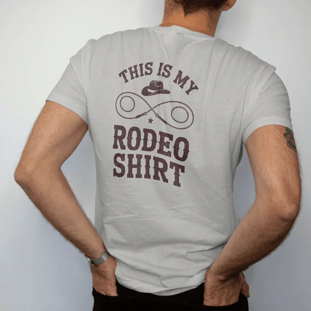 Man wearing a Granite tee, seen from the back: a pair of crossed lassos with a single hat and a small star above, "THIS IS MY" in small retro 70s caps and "RODEO SHIRT" in big chunky 70s slab letters below, in a faded 1970s souvenir style with a…
