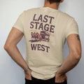 Man wearing a Sandstone tee, seen from the back: a stagecoach pulled by four horses across the desert with dust trailing behind, "LAST STAGE" in faded Tuscan rodeo-poster letters above and "WEST" small below, in a faded 1970s souvenir style with a…
