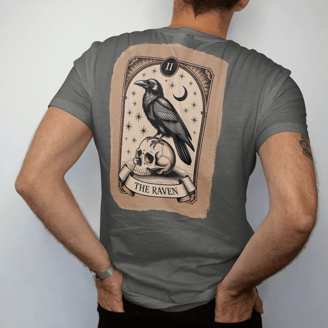 Man wearing a Pepper tee, seen from the back: back print: raven perched on a skull inside an ornate tarot-card frame with stars and a crescent moon, fine Victorian engraving style, "THE RAVEN" on a banner at the bottom in elegant high-contrast…