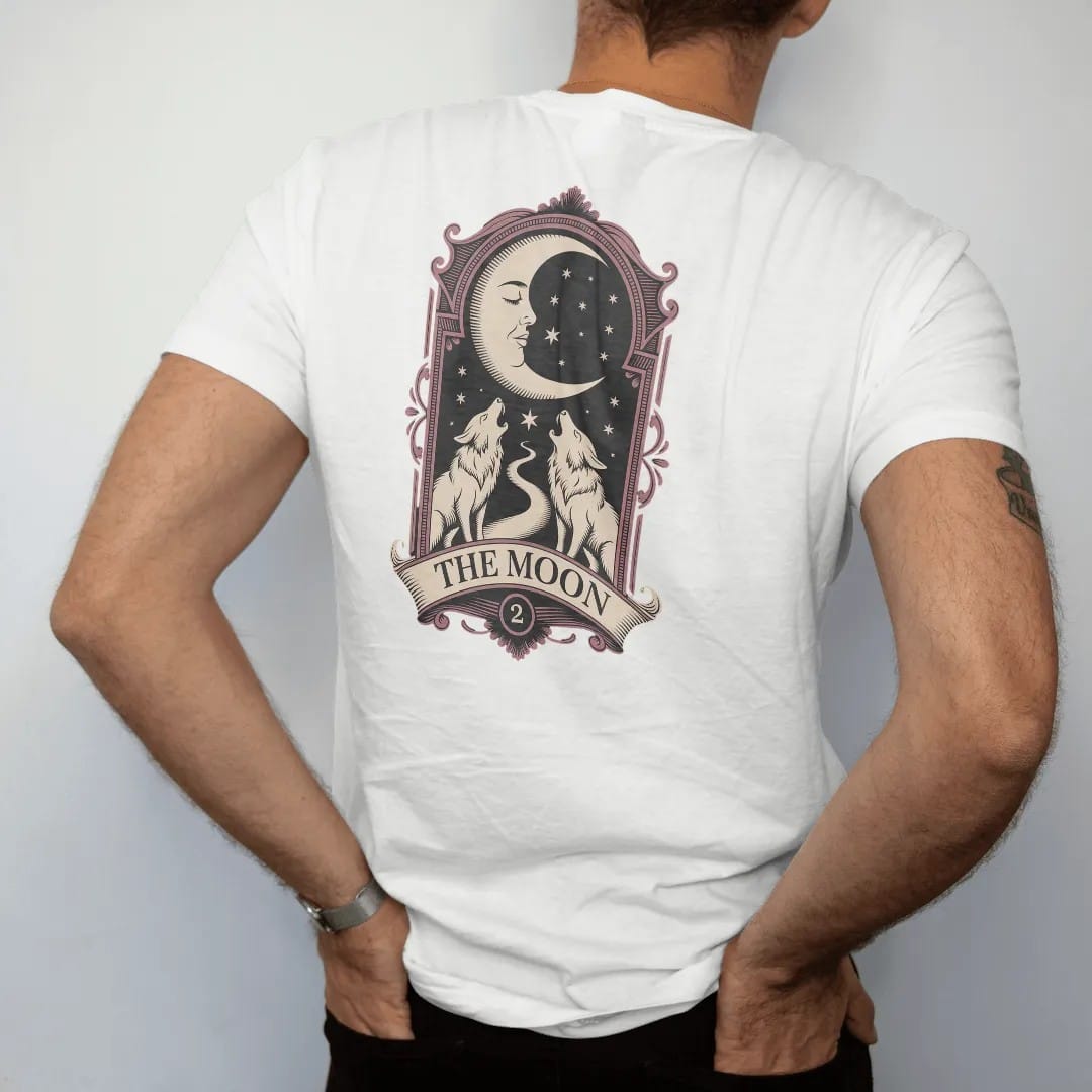 Man wearing a White tee, seen from the back: back print: crescent moon with a sleeping face above two howling wolves and a winding path inside an ornate tarot-card frame, detailed engraving style, "THE MOON" on a banner below in elegant…