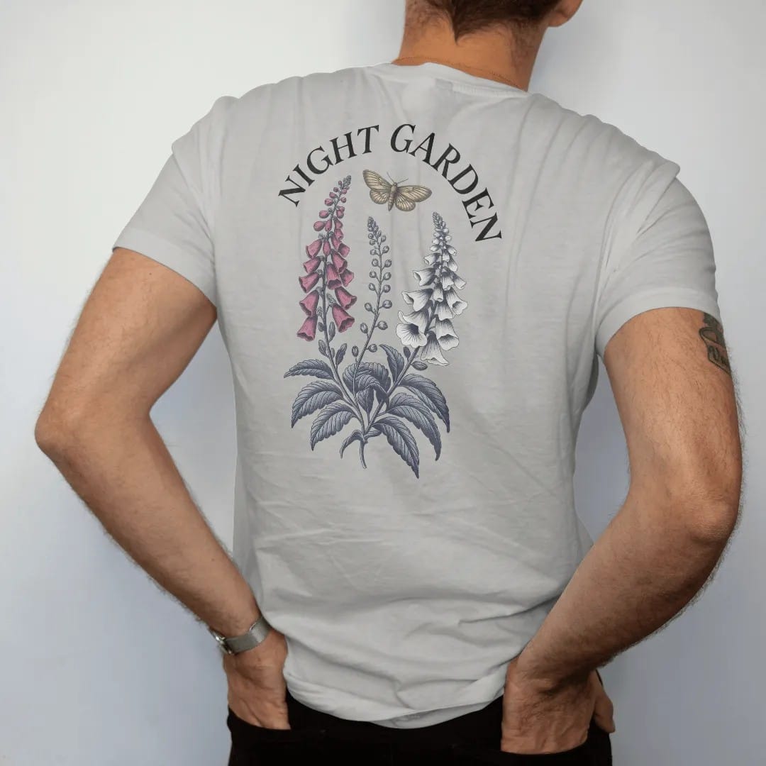 Man wearing a Granite tee, seen from the back: back print: botanical plate of nightshade, foxglove and moonflowers with a moth hovering, antique botanical engraving style, "NIGHT GARDEN" curved above in elegant high-contrast serif caps, printed in…
