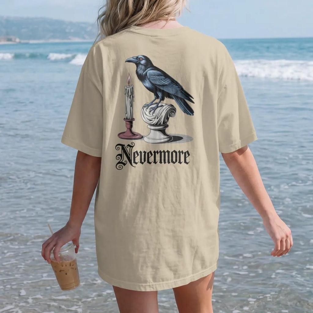 Woman on the beach in a Sandstone tee, back view: back print: raven perched on a classical marble bust beside a guttering candle, detailed Victorian engraving style, "NEVERMORE" below in ornate gothic blackletter, printed in bone cream, antique…
