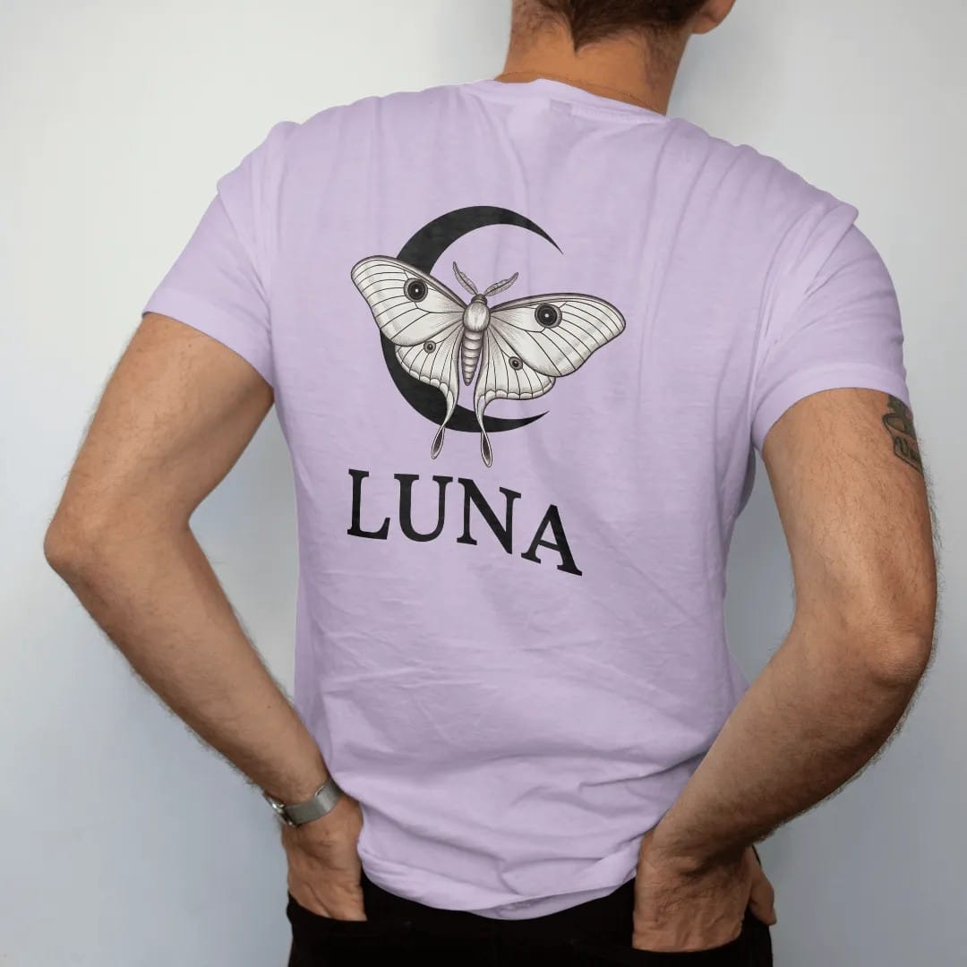 Man wearing a Orchid tee, seen from the back: back print: luna moth with long trailing wing tails over a crescent moon, delicate naturalist engraving style, "LUNA" below in elegant high-contrast serif caps with wide tracking, printed in ink black,…