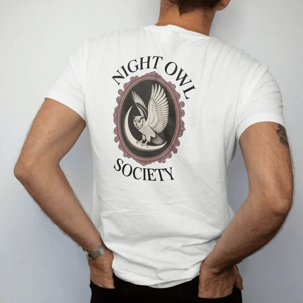 Man wearing a White tee, seen from the back: back print: great horned owl with spread wings on a crescent moon inside an ornate oval frame, detailed Victorian engraving, "NIGHT OWL" arched above in elegant high-contrast serif caps, "SOCIETY" below…