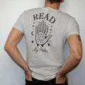 Man wearing a Granite tee, seen from the back: back print: open palm covered in palmistry lines, moons and stars, vintage fortune-teller chart style engraving, "READ" above in elegant high-contrast serif caps, "MY PALM" below in thin copperplate…