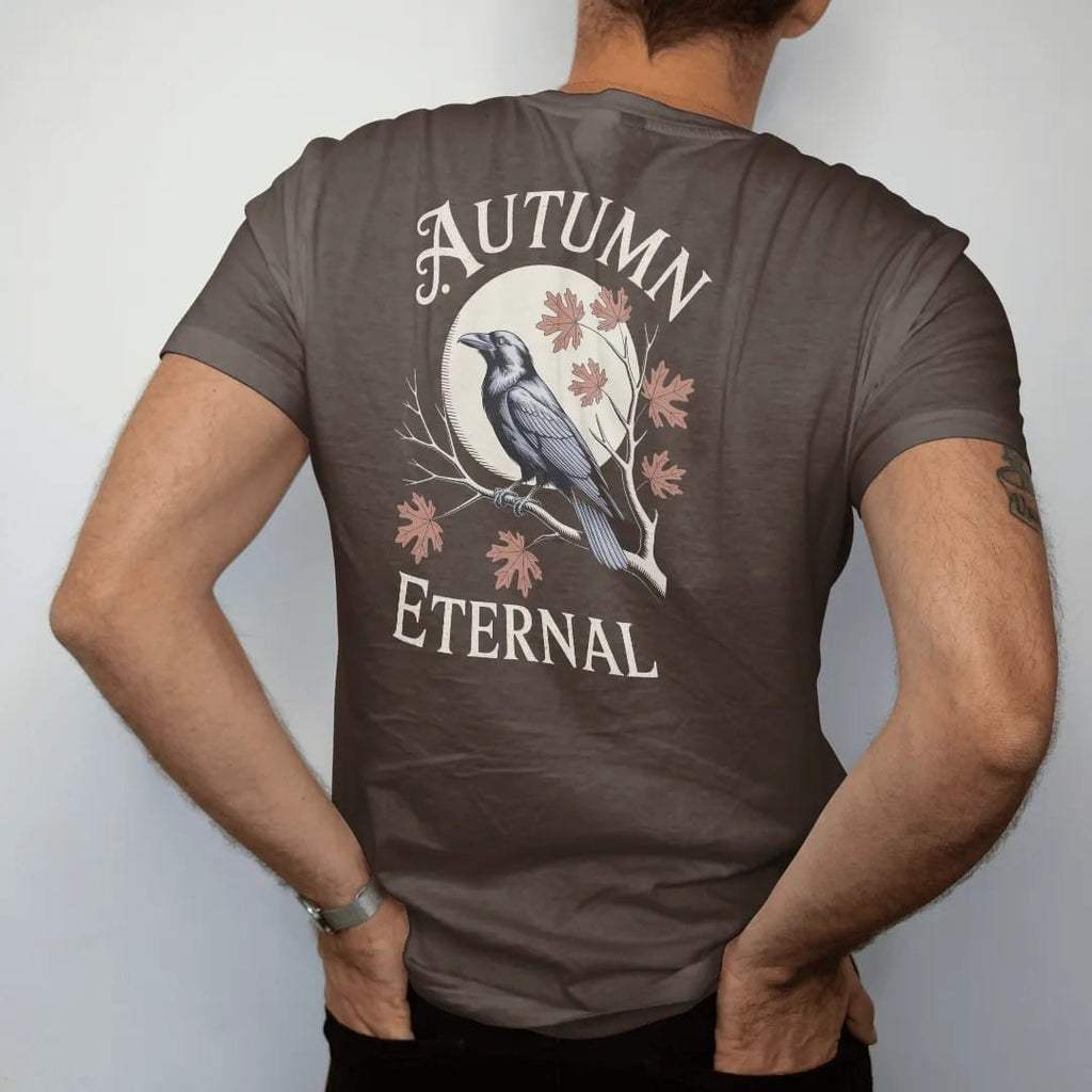 Man wearing a Espresso tee, seen from the back: back print: raven on a bare branch with oak and maple leaves drifting down past a harvest moon, fine engraving style, "AUTUMN" above in ornate gothic blackletter, "ETERNAL" below in small tracked…