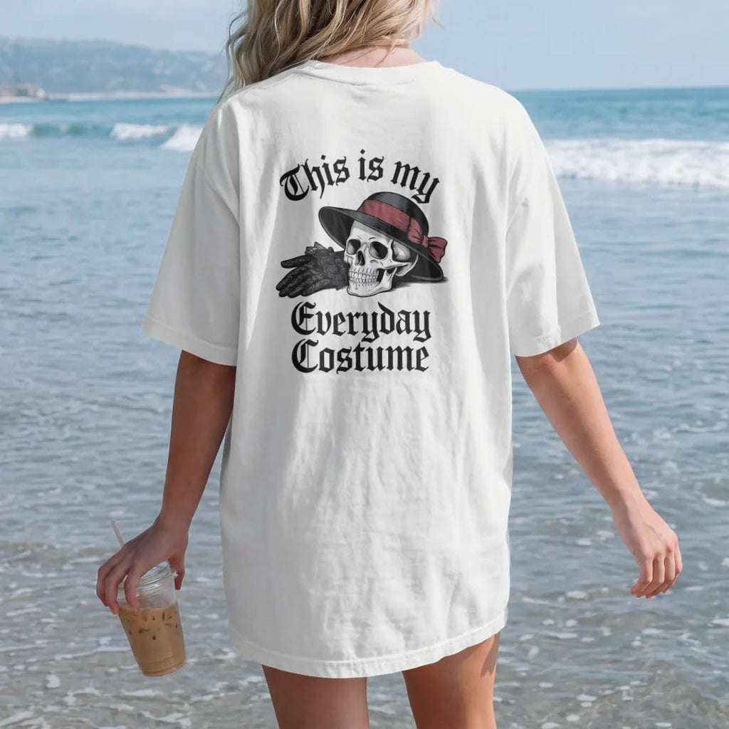 Woman on the beach in a White tee, back view: back print: pair of black lace gloves and a veiled hat beside a small skull, Victorian fashion-plate engraving, "THIS IS MY" above in thin copperplate script, "EVERYDAY" in ornate blackletter, "COSTUME"…