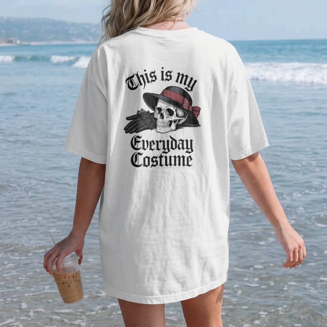 Woman on the beach in a White tee, back view: back print: pair of black lace gloves and a veiled hat beside a small skull, Victorian fashion-plate engraving, "THIS IS MY" above in thin copperplate script, "EVERYDAY" in ornate blackletter, "COSTUME"…