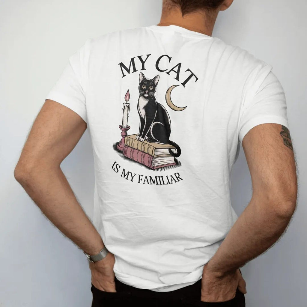 Man wearing a White tee, seen from the back: back print: black cat sitting on a stack of old books with a crescent moon and candle, fine Victorian engraving style, "MY CAT" above in elegant high-contrast serif caps, "IS MY FAMILIAR" below in thin…
