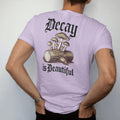 Man wearing a Orchid tee, seen from the back: back print: cluster of wild mushrooms and moss growing from a fallen log with a beetle, antique botanical engraving, "DECAY" above in ornate gothic blackletter, "IS BEAUTIFUL" below in thin copperplate…