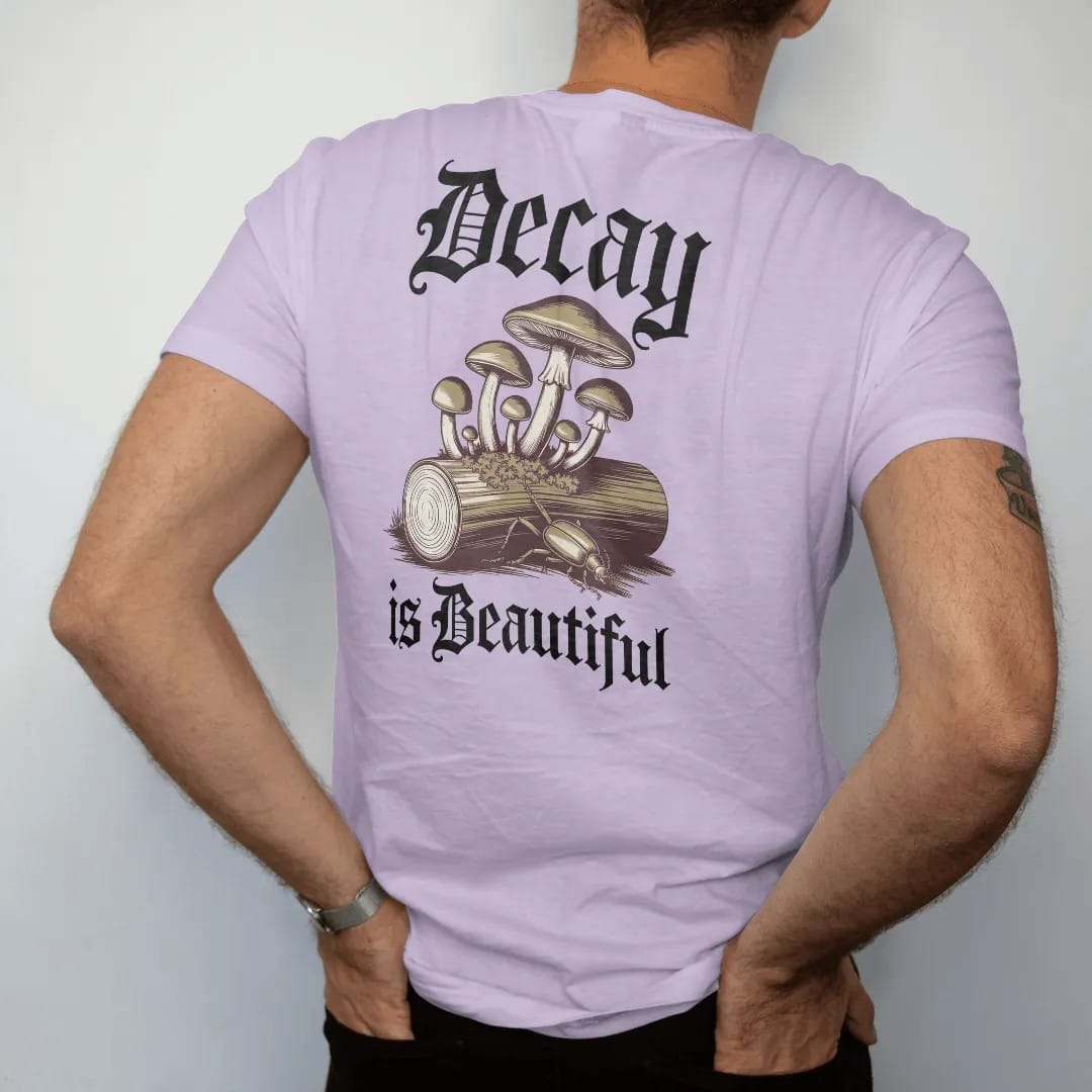 Man wearing a Orchid tee, seen from the back: back print: cluster of wild mushrooms and moss growing from a fallen log with a beetle, antique botanical engraving, "DECAY" above in ornate gothic blackletter, "IS BEAUTIFUL" below in thin copperplate…