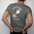 Man wearing a Pepper tee, seen from the back: back print: skeleton hand pouring tea from an ornate teapot into a cup with a moth on the saucer, Victorian engraving, "MIDNIGHT" above in elegant high-contrast serif caps, "TEA SERVICE" below in thin…