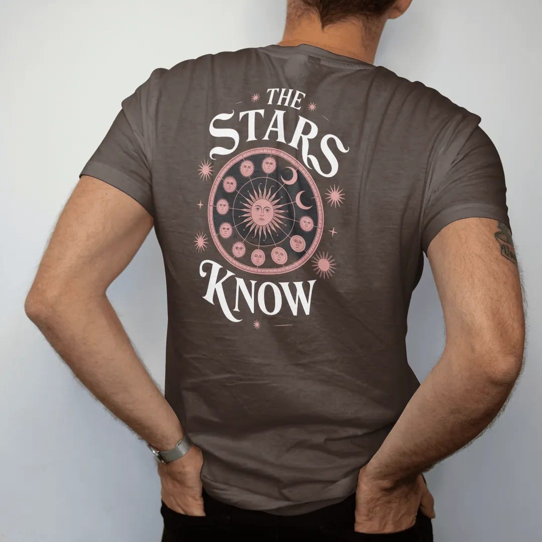 Man wearing a Espresso tee, seen from the back: back print: antique zodiac wheel with constellations, sun and moon faces in a celestial engraving style, "THE" small above, "STARS" in ornate gothic blackletter, "KNOW" below in elegant high-contrast…