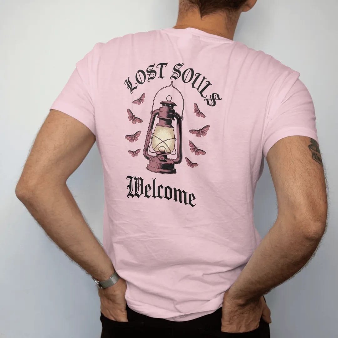 Man wearing a Blossom tee, seen from the back: back print: old iron lantern glowing on a hook with moths circling the light, Victorian engraving with stippled glow, "LOST SOULS" arched above in ornate gothic blackletter, "WELCOME" below in thin…