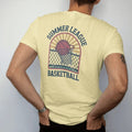 Man wearing a Butter tee, seen from the back: a vintage basketball swishing through a chain-link net on an outdoor court with sun rays, with "SUMMER LEAGUE" and "BASKETBALL" in chunky 1970s swash script, printed in faded varsity navy, washed red,…
