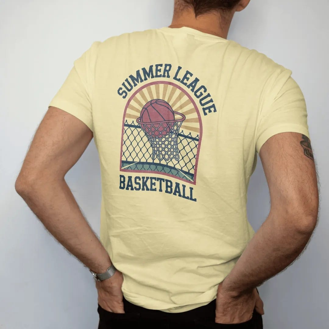Man wearing a Butter tee, seen from the back: a vintage basketball swishing through a chain-link net on an outdoor court with sun rays, with "SUMMER LEAGUE" and "BASKETBALL" in chunky 1970s swash script, printed in faded varsity navy, washed red,…