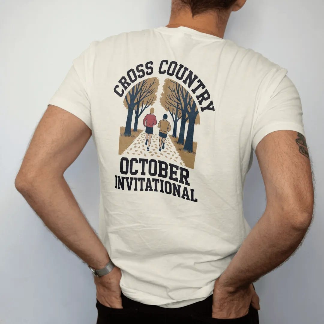 Man wearing a Ivory tee, seen from the back: two runners on a leaf-covered trail through autumn trees, with "CROSS COUNTRY" and "OCTOBER INVITATIONAL" in chunky faded collegiate block letters, printed in faded varsity navy, washed red, mustard gold…