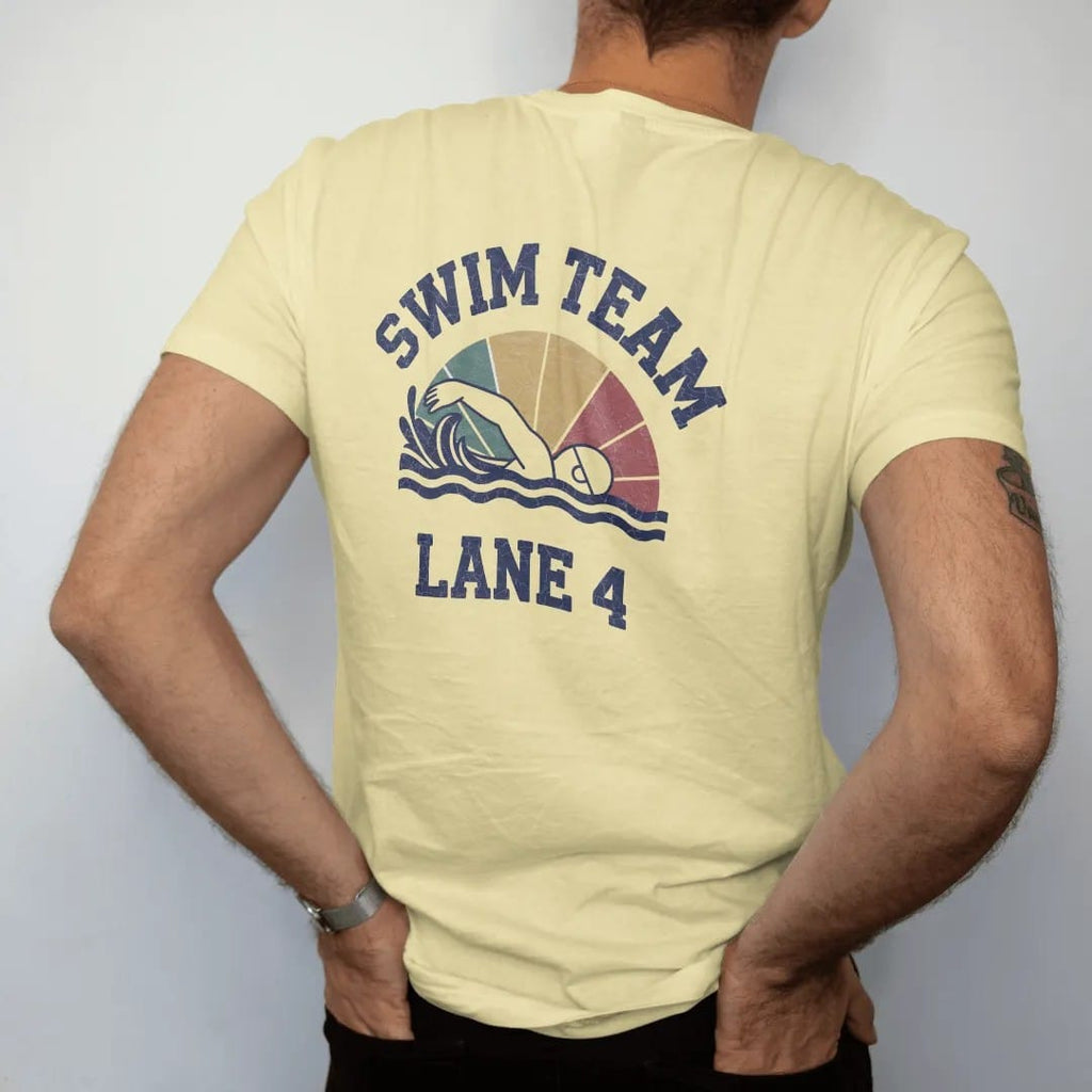 Man wearing a Butter tee, seen from the back: a swimmer mid freestyle stroke with stylized splashing waves and a lane rope, with "SWIM TEAM" and "LANE 4" in chunky faded collegiate block letters, printed in faded varsity navy, washed red, mustard…