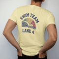 Man wearing a Butter tee, seen from the back: a swimmer mid freestyle stroke with stylized splashing waves and a lane rope, with "SWIM TEAM" and "LANE 4" in chunky faded collegiate block letters, printed in faded varsity navy, washed red, mustard…
