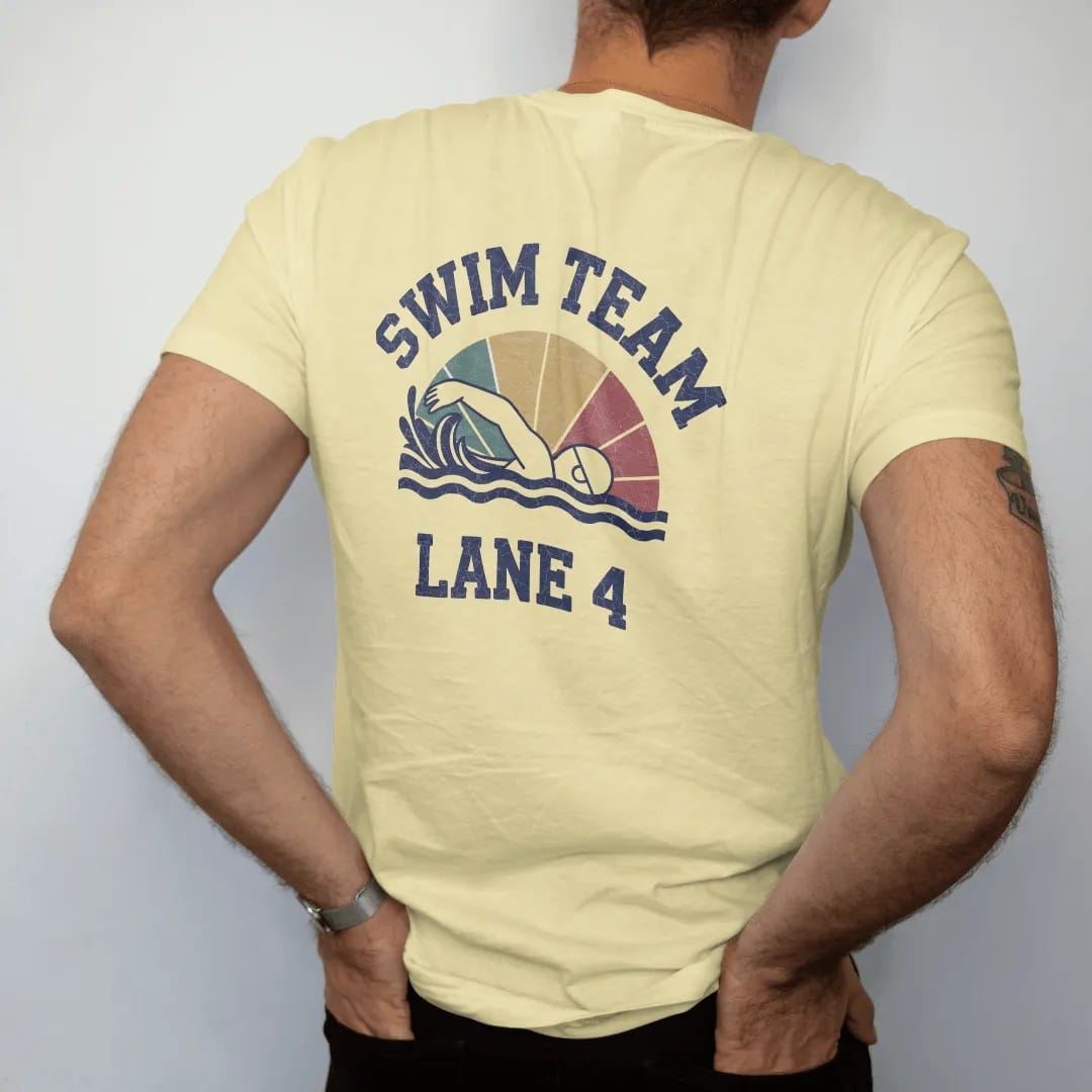Man wearing a Butter tee, seen from the back: a swimmer mid freestyle stroke with stylized splashing waves and a lane rope, with "SWIM TEAM" and "LANE 4" in chunky faded collegiate block letters, printed in faded varsity navy, washed red, mustard…