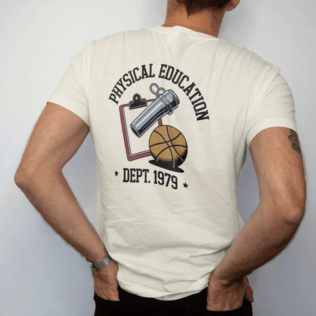 Man wearing a Ivory tee, seen from the back: a chrome whistle on a lanyard over a clipboard and a rubber playground ball, with "PHYSICAL EDUCATION" and "DEPT. 1979" in chunky faded collegiate block letters, printed in faded varsity navy, washed…