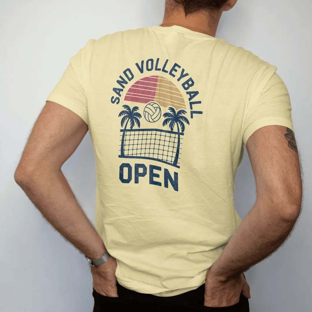 Man wearing a Butter tee, seen from the back: a volleyball being spiked over a net with a sun and palm trees, with "SAND VOLLEYBALL" and "OPEN" in chunky 1970s swash script, printed in faded varsity navy, washed red, mustard gold and pine green…