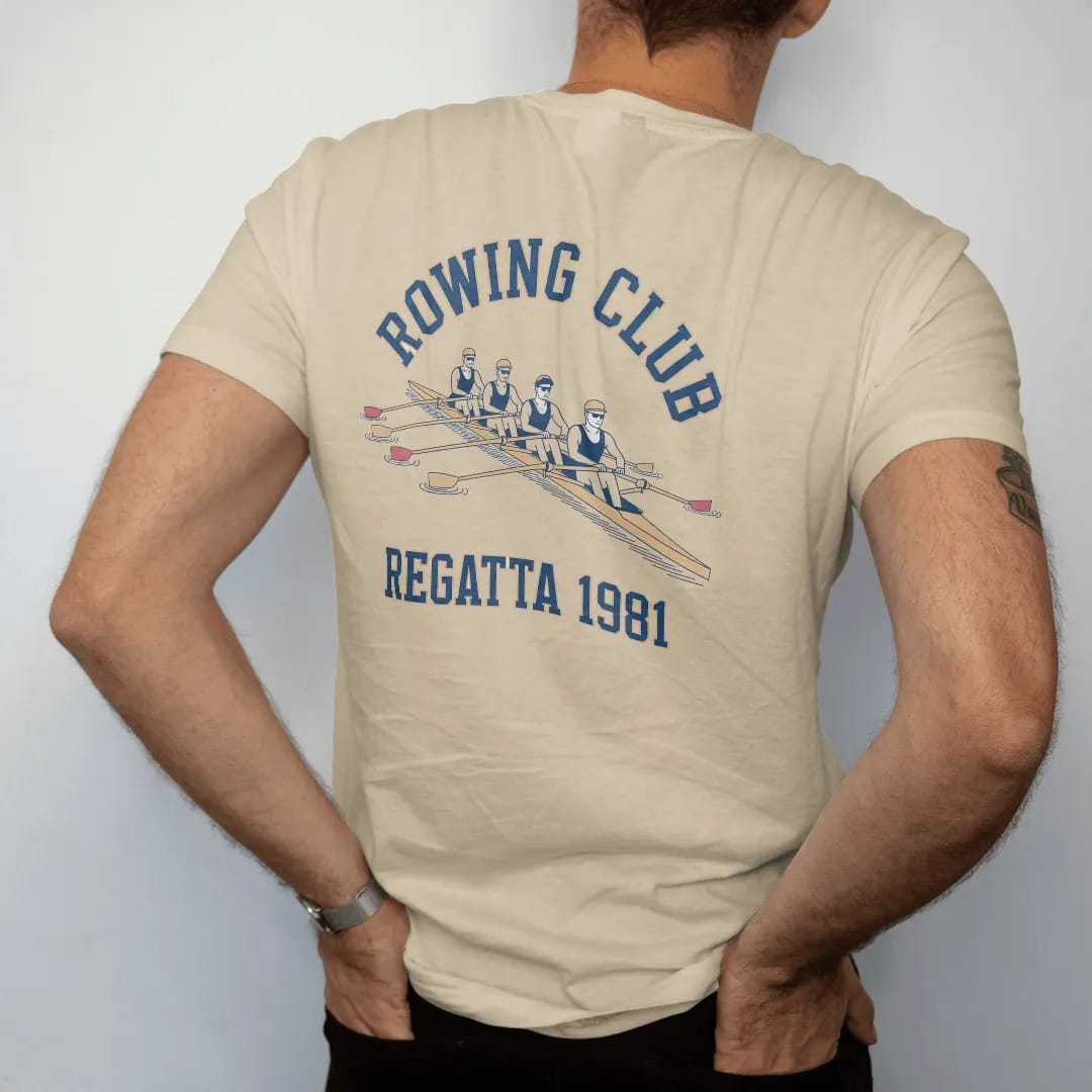 Man wearing a Sandstone tee, seen from the back: a long rowing shell with four rowers pulling in sync on rippled water, with "ROWING CLUB" and "REGATTA 1981" in chunky faded collegiate block letters, printed in faded varsity navy, washed red,…