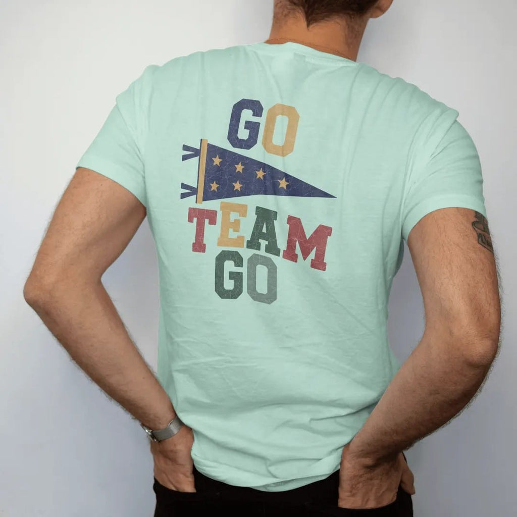 Man wearing a Chalky Mint tee, seen from the back: a classic felt pennant waving on a stick with stars, with "GO TEAM GO" in chunky rounded 70s block letters, printed in faded varsity navy, washed red, mustard gold and pine green with a cracked,…