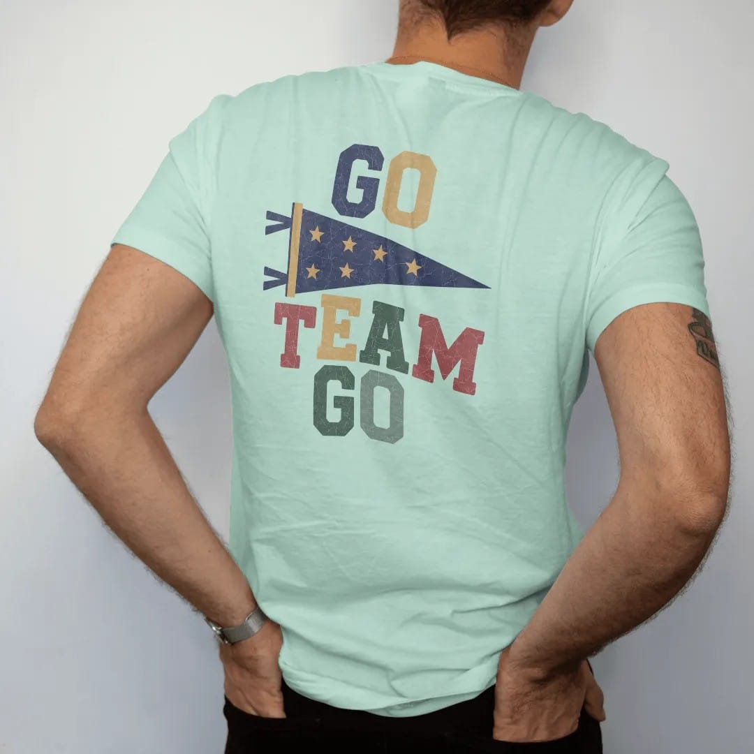Man wearing a Chalky Mint tee, seen from the back: a classic felt pennant waving on a stick with stars, with "GO TEAM GO" in chunky rounded 70s block letters, printed in faded varsity navy, washed red, mustard gold and pine green with a cracked,…