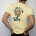 Man wearing a Butter tee, seen from the back: a softball and leather glove with dirt puffs, with "SLOW PITCH" and "SOFTBALL LEAGUE" in chunky 1970s swash script, printed in faded varsity navy, washed red, mustard gold and pine green with a cracked,…