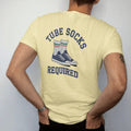 Man wearing a Butter tee, seen from the back: a pair of striped tube socks pulled high over sneakers, with "TUBE SOCKS" and "REQUIRED" in chunky rounded 70s block letters, printed in faded varsity navy, washed red, mustard gold and pine green with…