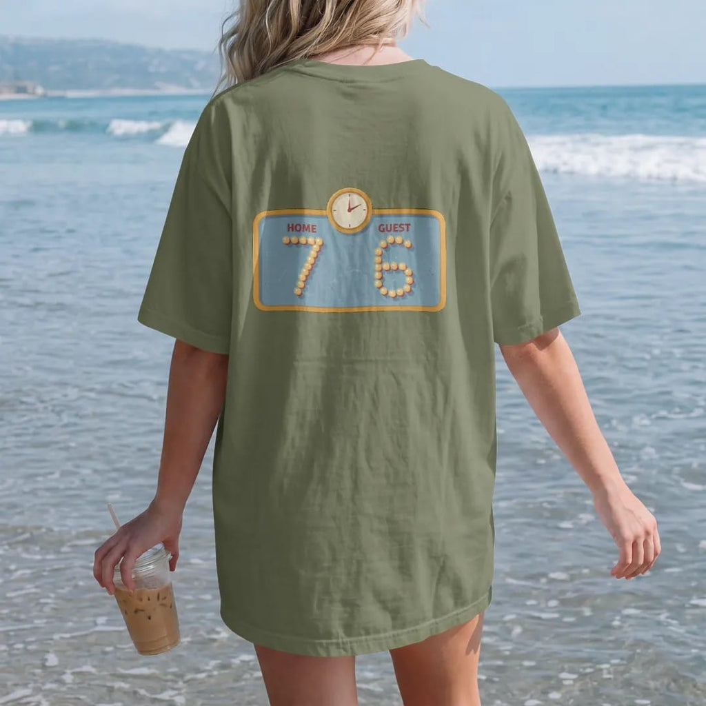 Woman on the beach in a Moss tee, back view: a vintage light-bulb scoreboard with a small clock, with "HOME 7" and "GUEST 6" in light-bulb scoreboard digits, printed in faded bleacher cream, mustard gold, washed red and dusty sky blue with a…