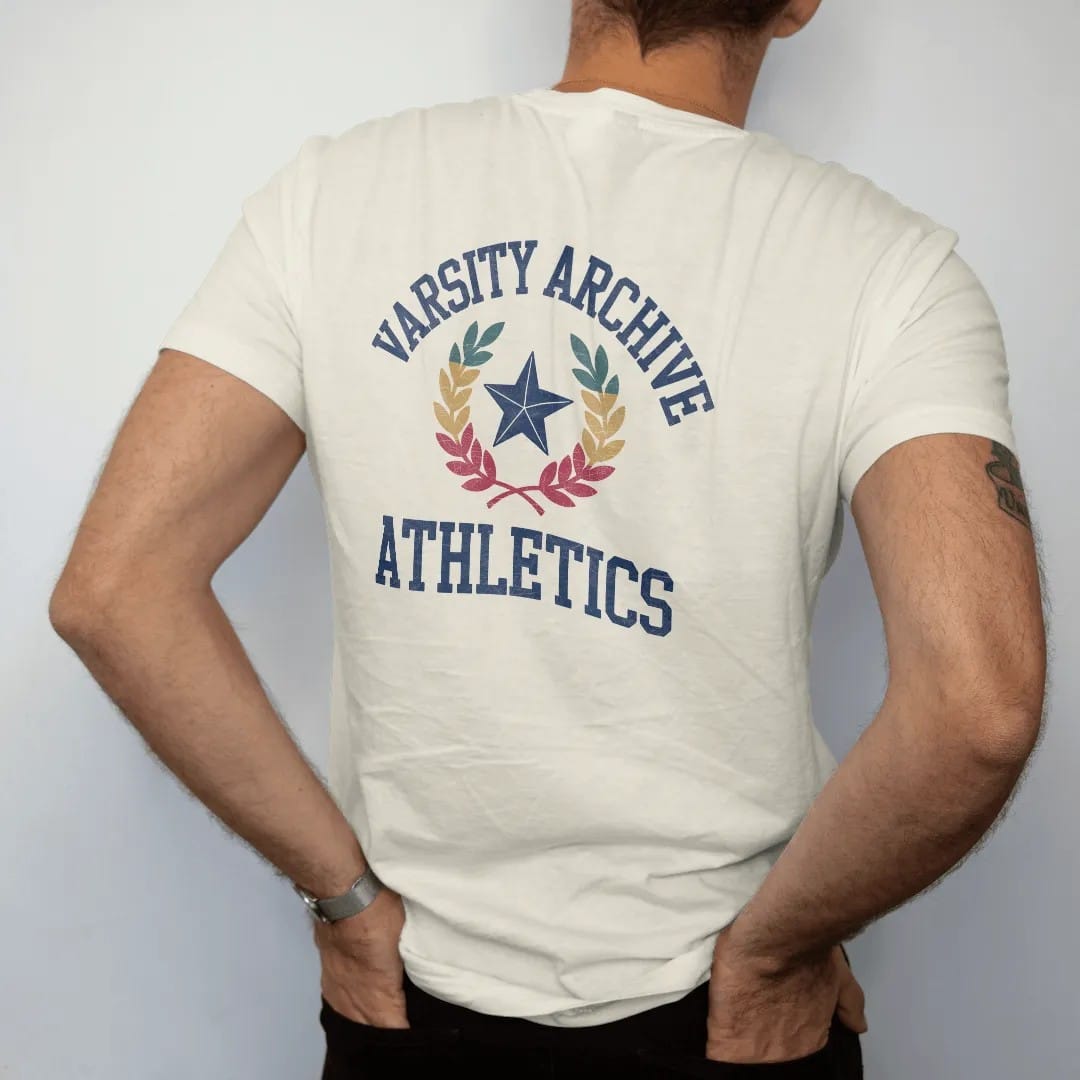 Man wearing a Ivory tee, seen from the back: a chenille letterman patch with a star and crossed laurel branches, with "VARSITY ARCHIVE" and "ATHLETICS" in chunky faded collegiate block letters, printed in faded varsity navy, washed red, mustard…