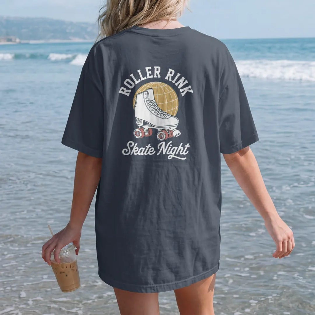Woman on the beach in a Midnight tee, back view: a classic quad roller skate with striped laces under a mirror ball, with "ROLLER RINK" and "SKATE NIGHT" in chunky 1970s swash script, printed in faded bleacher cream, mustard gold, washed red and…