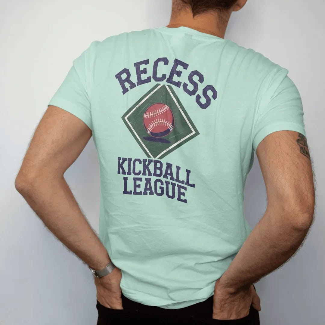 Man wearing a Chalky Mint tee, seen from the back: a bouncing red kickball over a chalk-drawn diamond, with "RECESS" and "KICKBALL LEAGUE" in chunky rounded 70s block letters, printed in faded varsity navy, washed red, mustard gold and pine green…