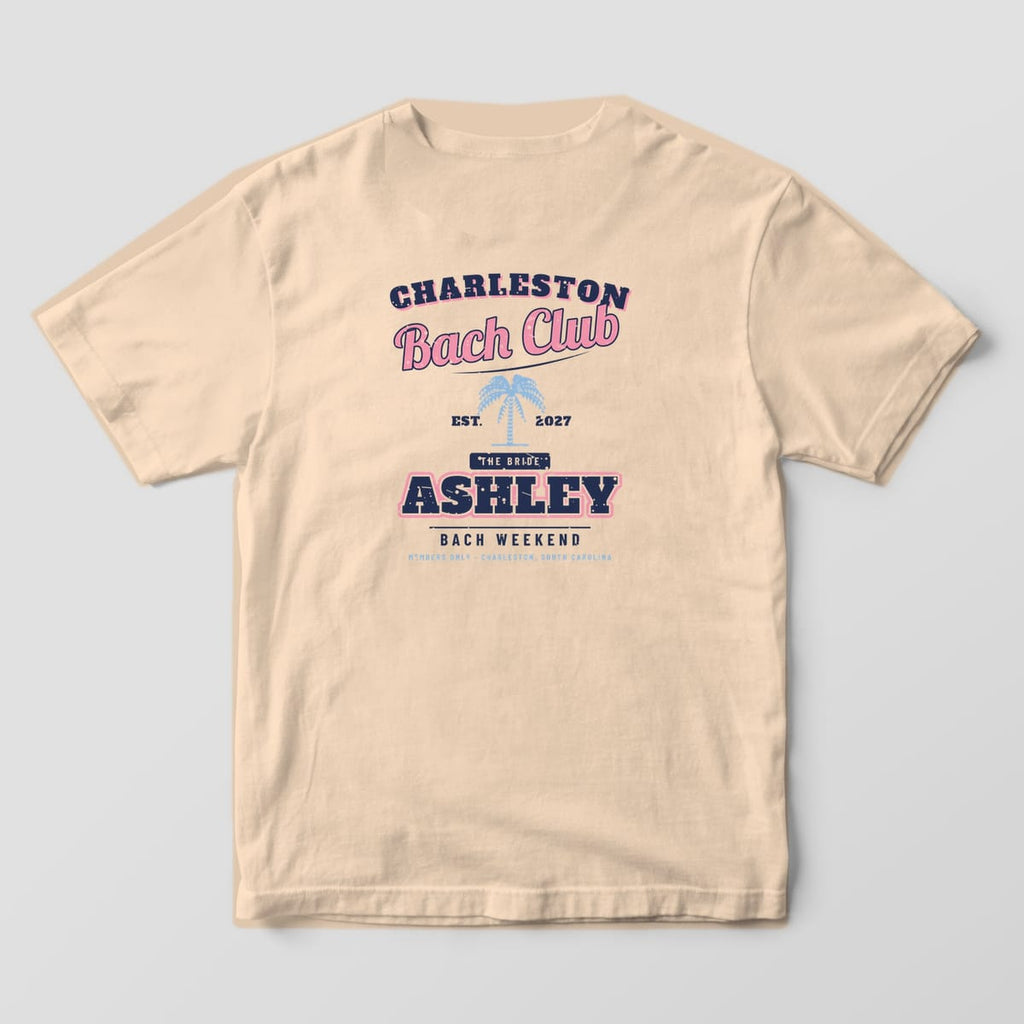 Back of an ivory Comfort Colors 1717 tee: arched CHARLESTON, pink Bach Club script, palmetto, EST. 2027, THE BRIDE tab and ASHLEY. A CREW version is also offered.