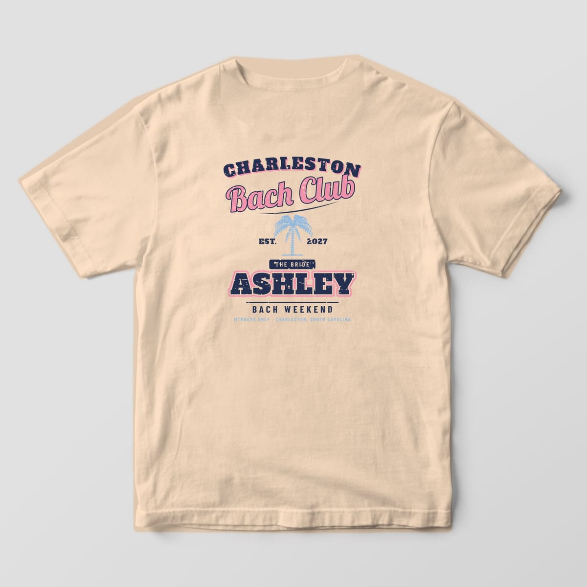 Back of an ivory Comfort Colors 1717 tee: arched CHARLESTON, pink Bach Club script, palmetto, EST. 2027, THE BRIDE tab and ASHLEY. A CREW version is also offered.