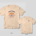 Ivory Comfort Colors tee with a retro back print of a champagne coupe over a striped sunset and waves, reading Last Toast on the Coast, plus a chest print inset.