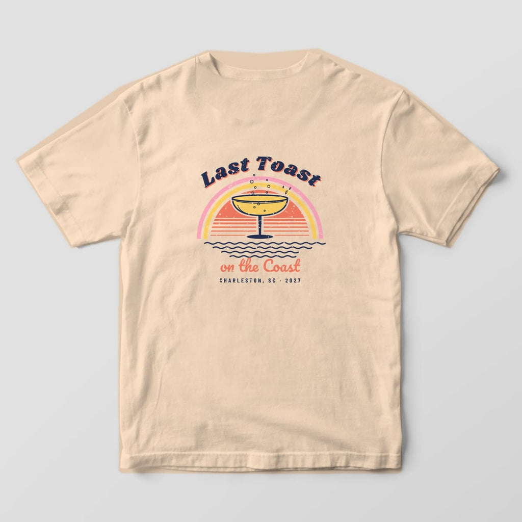 Back of an ivory Comfort Colors 1717 tee: Last Toast arched over a pink and yellow rainbow, coral sunset, coupe glass, navy waves and Charleston, SC 2027.