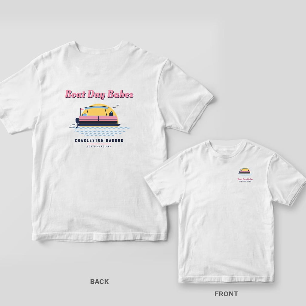 White Comfort Colors tee with a back print of a pink and navy pontoon boat under a yellow sun reading Boat Day Babes, Charleston Harbor, plus a chest print inset.