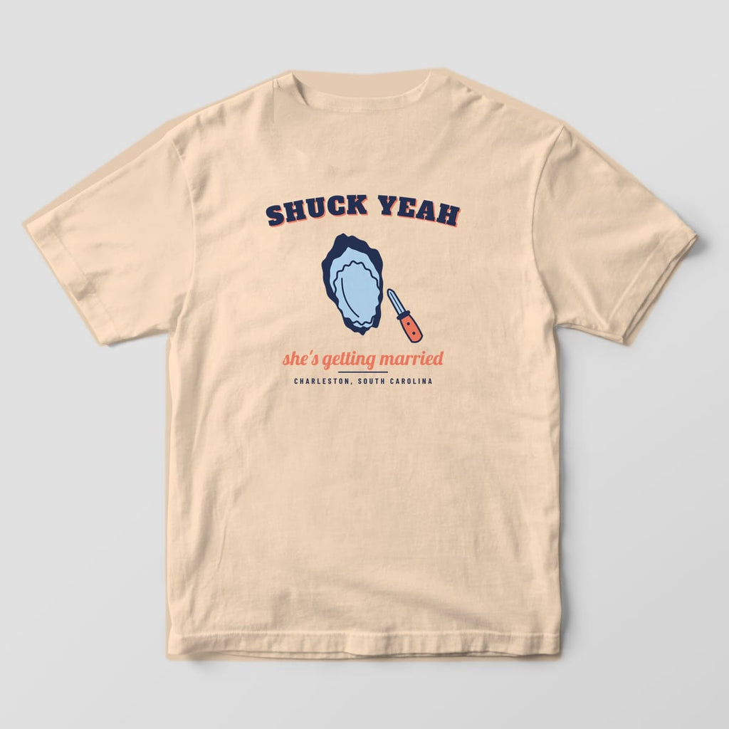 Back of an ivory Comfort Colors 1717 tee with arched navy SHUCK YEAH, a blue and navy oyster, a coral-handled knife and Charleston, South Carolina.