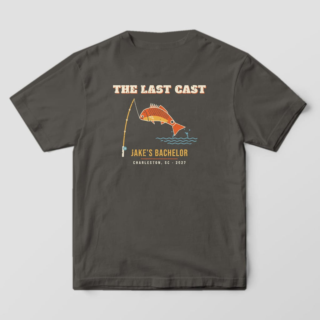 Back of a pepper Comfort Colors 1717 tee with cream THE LAST CAST lettering, an orange and gold redfish, teal waves and JAKE'S BACHELOR in gold.