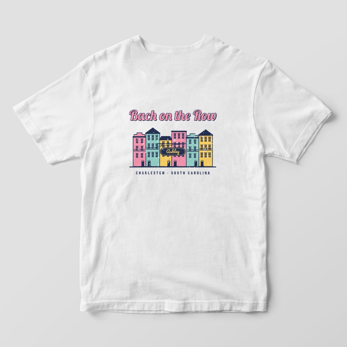 Back of a white Comfort Colors 1717 tee with six pink, mint and yellow row houses with balconies and fanlight doors, a navy sign reading Ashley and Charleston, South Carolina.