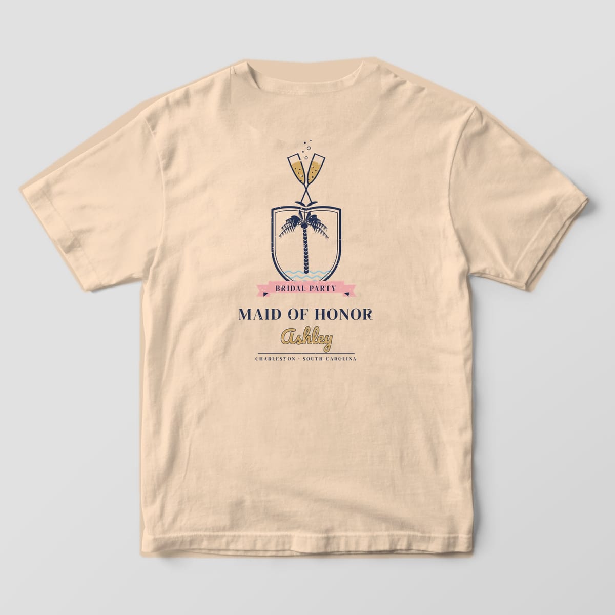 Back of an Ivory Comfort Colors tee with a crest of crossed champagne flutes over a palmetto shield, BRIDAL PARTY ribbon and personalized role and name
