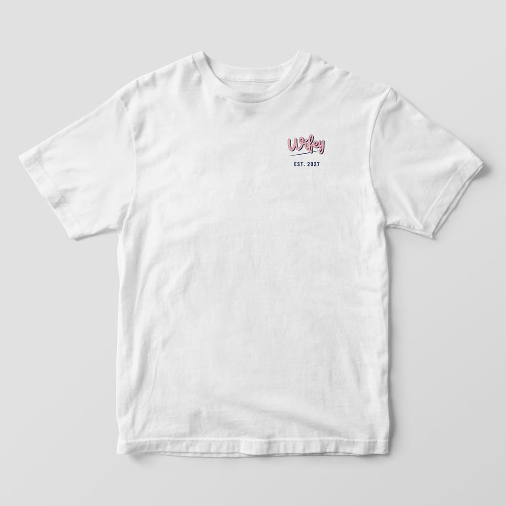 Front of a White Comfort Colors tee with a small Wifey script and EST. 2027 on the left chest