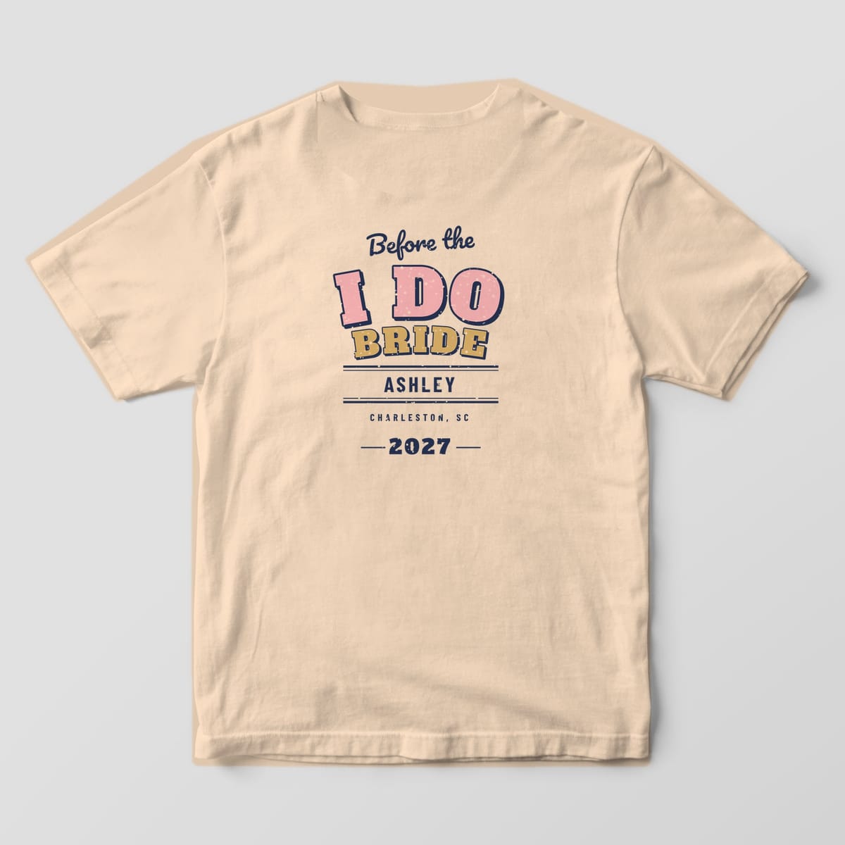 Back of an Ivory Comfort Colors tee: Before the script over arched pink I DO, gold BRIDE, ASHLEY between navy stripes and 2027